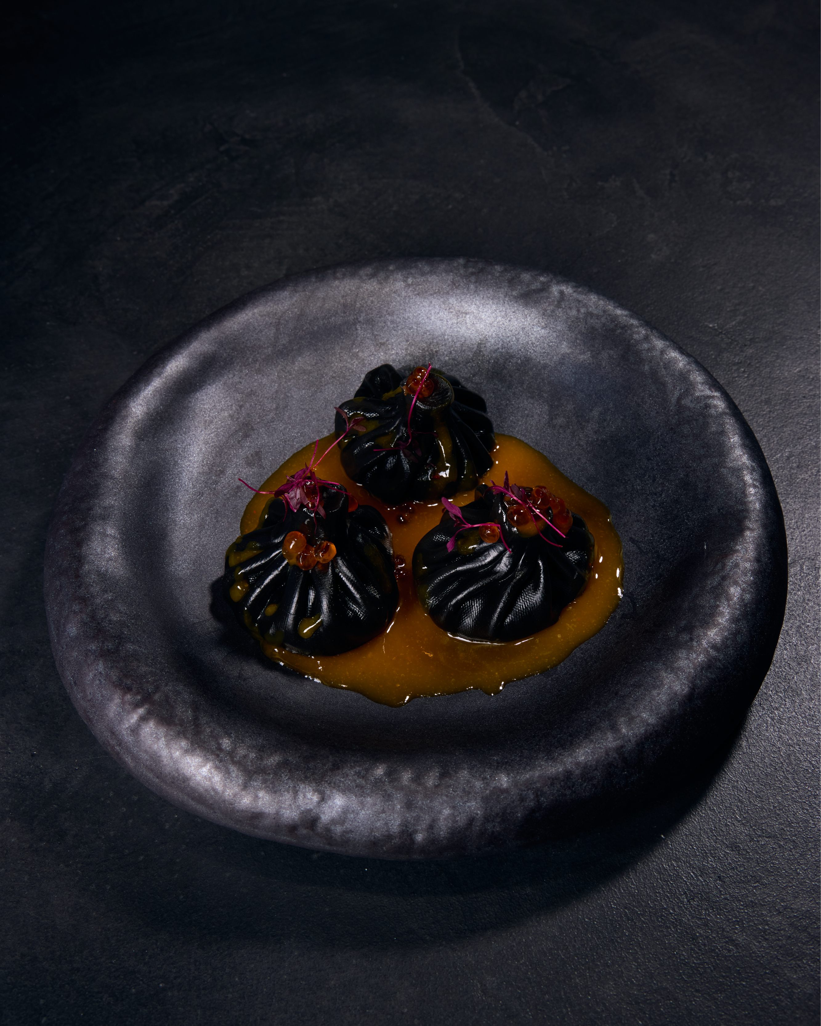 Black dumplings on plate with sauce.