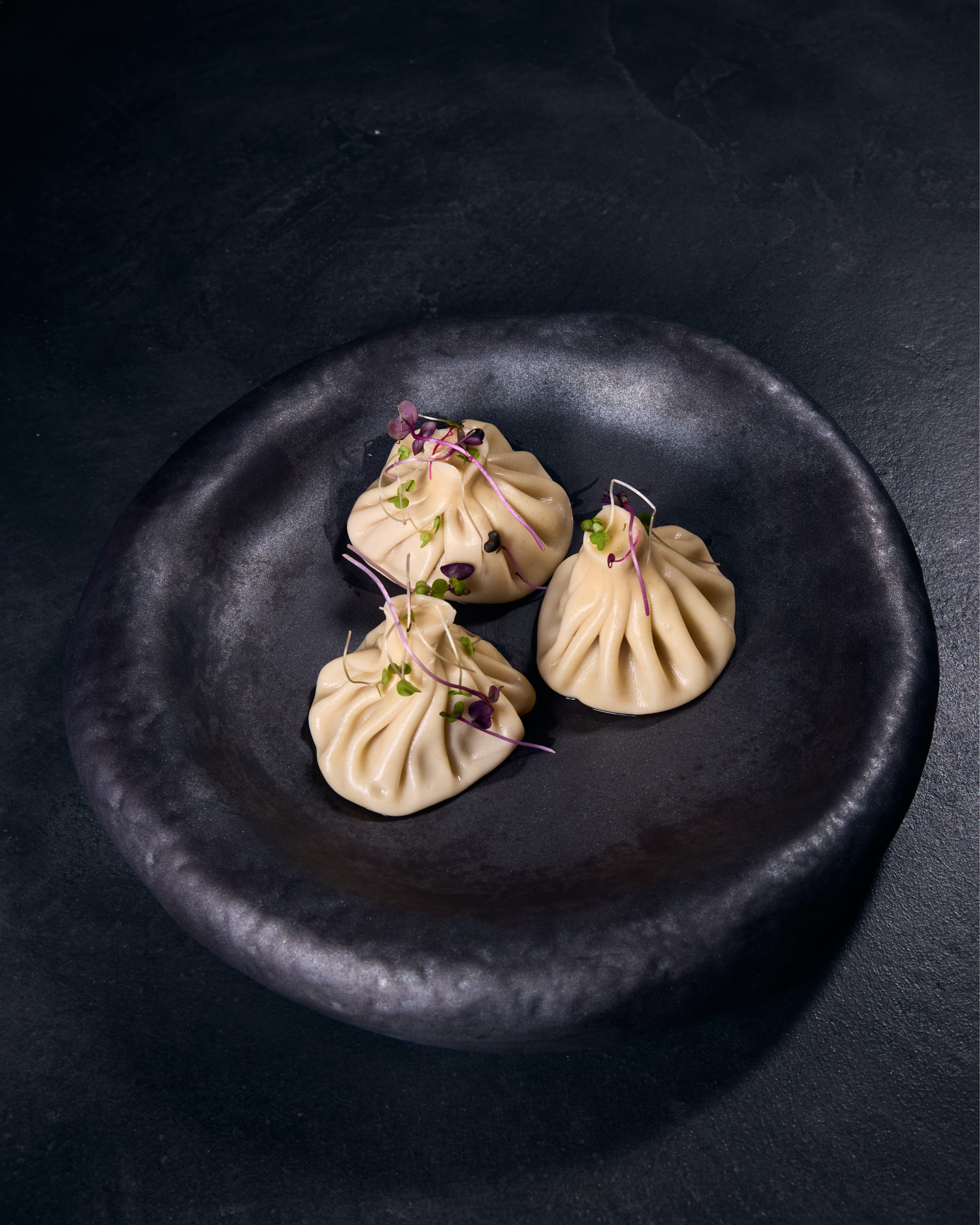 Three dumplings garnished on black plate.