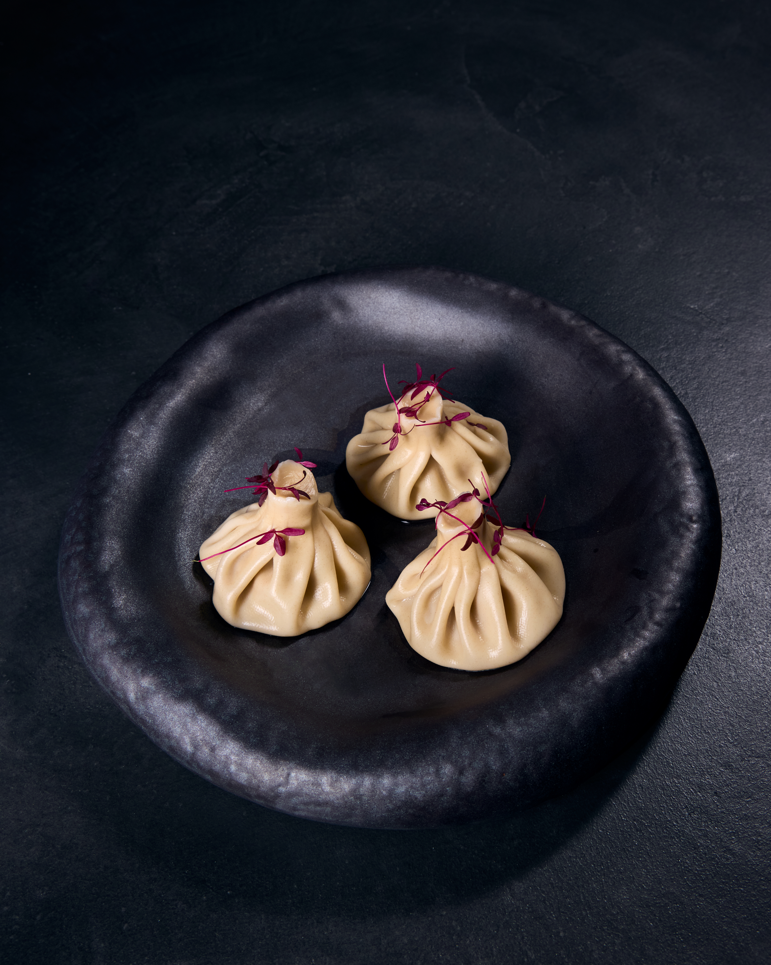 Three dumplings on a black plate.